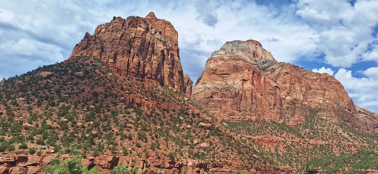 Red sandstone peaks rising above a juniper-covered slope in southern Utah, with clouds overhead.